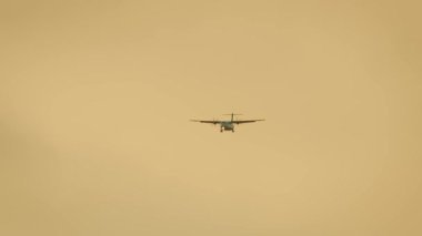 Turbo pervane sıcak akşam tonlarıyla altın gökyüzünde uçuyor. Bölgesel uçak gün batımı atmosferi altında ilerliyor. Pervane düzlemi turuncu arka planda iniyor. Alacakaranlık vakti, küçük yolcu uçakları alçak irtifaya yaklaşıyor.