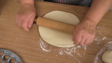 Masada ahşap broşla yuvarlanan hamur. Tanınmayan kişi yuvarlak hamuru düzleştiriyor. Yumuşak hamuru ince tabakaya yaymak. Ev yapımı hamur tatlısı için temel hazırlanıyor.