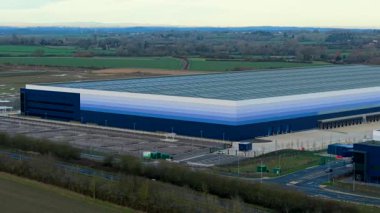 Kırsal sanayi bölgesindeki büyük deponun lojistik işletim süreçlerinin havadan görüntüsü. Devasa dağıtım merkezinin insansız hava aracı perspektifi depolama ve tedarik zinciri çalışmalarını yönetiyor. Modern lojistiğin yüksek irtifa görünümü