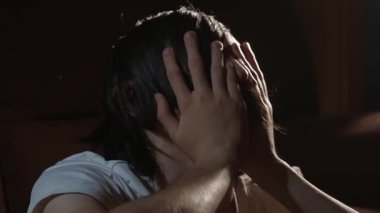 Elleriyle yüzünü kapatan genç adam yoğun bir duygusal sıkıntı ve endişe hissediyor. Kafa tutan kişi artan tansiyon ve ezici iç basınç gösteriyor. Yüzü saklanan genç derin psikolojik mücadele ve yorgunluğu yansıtıyor.