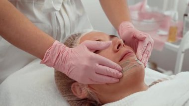 Kozmetik kliniğindeki güzellik uzmanından yüz masajı alan hasta rahat yüzüyle yatıyor. Güzellik uzmanının hastaya cilt bakımı uygulaması sakin ve rahatlatıcı bir deneyim sağlıyor. Uzman güzellik uzmanları tarafından yüz terapisi gören hasta...