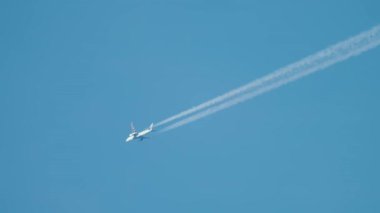 Mavi gökyüzünde uçan yolcu uçağı seyir irtifasında. Jet uçakları beyaz kontrastlar bırakarak uzun kimyasal izler oluşturuyor. Zararlı emisyonlar yayan ticari uçak iklim değişikliğini etkiliyor