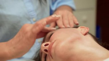 Rahatlamak ve rahatlamak için alnına masaj yapmak. Terapist yüz masajı için çalışıyor. Gençleşmek için profesyonel bir alın. Uyum için ruhsal tedavi sağlama uzmanı