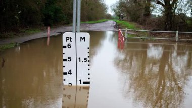 Su seviyesi göstergesi, sualtı kırsal yolda yükselen suyu gösteriyor. Kahverengi taşkın suyu kaldırımı kaplıyor ve yoğun yağmurdan sonra artıyor. Şiddetli hava koşulları yoğunlaşıyor ve kırsal altyapı boyunca tehlikeli taşkınlıklara yol açıyor.