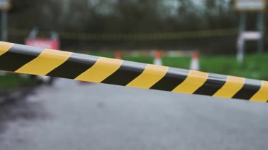 Kapalı yol boyunca uzanan siyah ve sarı uyarı bandı. Kapalı tabela ve trafik konileri arka planda erişimi engelliyor. Geçici kısıtlama araç girişini engelliyor ve trafik hareketini kısıtlıyor