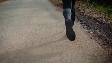 Parkın asfalt yolunda koşan bacaklara yakından bakın. Spor ayakkabıları ve spor aletleri açık hava koşusu sırasında hareket ediyor. Hareketli ama yorgun koşucu yoğun kardiyo eğitiminden sonra terliyor.