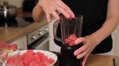 Karpuz küplerini karıştırıcı kavanoza koyuyorum. Taze kırmızı meyvelerle dolu bir kap. Meyve suyu ya da meyve suyu için malzeme hazırlıyorum. Mutfak tezgahında olgun kavun parçaları tutarak.