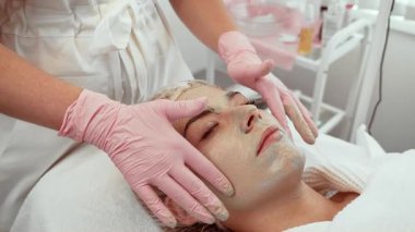 Güzellik uzmanı cilt temizleme yapıyor, tedavi sırasında kadının yüzüne nazikçe masaj yapıyor. Kadın sakince yatıyor, taze cilt için derin temizlik prosedürü uygulanıyor. Rahatlatıcı cilt bakımı yapan hasta yenilenme ve arınmaya odaklanıyor.