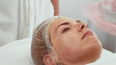 Cilt bakımı kliniğinde profesyonel tedaviden sonra temiz ve parlak bir ciltle yatan rahat bir kadın. Kadın yenilenmiş ve tazelenmiş görüntüden zevk alıyor. Hasta gelişmiş ışıltı için ileri yüz terapisini tamamladı.