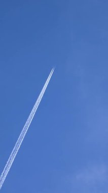 Şehirlerarası yolculuk sırasında açık mavi gökyüzünde uçan ticari uçak. Seyahat ve turizm konsepti tatil planlama ve tatil maceraları, dikey yönelim. Küresel keşif ve hava sahasında beyaz iz bırakan yolcu uçağı