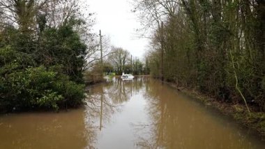 Şiddetli yağmur fırtınasından sonra neredeyse su altında kalmış bir araba. Şiddetli yağış, kırsal yol ve çevreleyen ağaçlar arasında derin ve durgun bir su yaratıyor. Şiddetli hava felaketi yol kapanmasına, araç hasarına ve ulaşım kaosuna yol açtı
