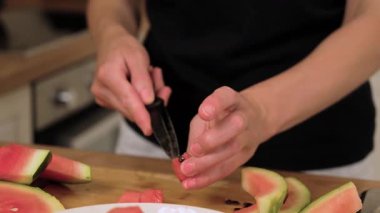 Karpuz küpünden siyah tohum çıkarıyorum. Bıçak ucunu kullanırken küçük bir parça tutuyor. Çekirdeksiz porsiyon servis ediliyor. Kesme tahtasındaki taze meyveyi tutuyorum.