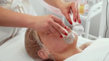 Kozmetik dermatoloji kliniğinde kadın yüzüne buz küreleri uyguluyor. Dişi, cilt tazeleme için soğutma tedavisinden zevk alıyor. Hasta alma terapisi rahatlama ve canlandırma üzerine odaklandı