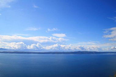 Mavi gökyüzü, denizin üstünde beyaz bulutlar