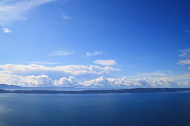 Mavi gökyüzü, denizin üstünde beyaz bulutlar