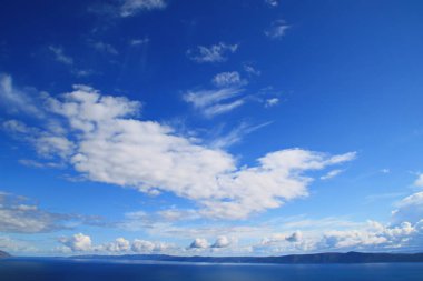 Mavi gökyüzü, denizin üstünde beyaz bulutlar