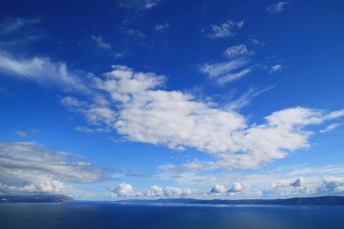 Mavi gökyüzü, denizin üstünde beyaz bulutlar