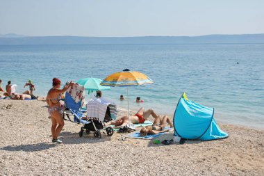 Podgora, Hırvatistan, 14.08.2021. Turistler, Polonya, Almanya, Macaristan, Çek Cumhuriyeti, Slovakya, Avusturya, Slovenya, Sırbistan ve Bosna-Hersek 'ten gelen turistlerin en sevdiği tatil beldesi olan Makarska Riviera, Podgora' daki plajın keyfini çıkarıyorlar.