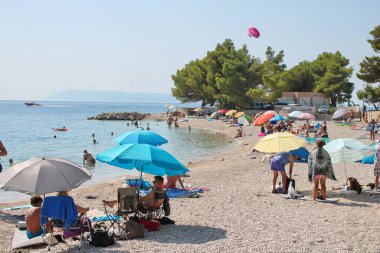 Podgora, Hırvatistan, 14.08.2021. Turistler, Polonya, Almanya, Macaristan, Çek Cumhuriyeti, Slovakya, Avusturya, Slovenya, Sırbistan ve Bosna-Hersek 'ten gelen turistlerin en sevdiği tatil beldesi olan Makarska Riviera, Podgora' daki plajın keyfini çıkarıyorlar.