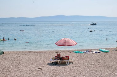Podgora, Hırvatistan, 14.08.2021. Turistler, Polonya, Almanya, Macaristan, Çek Cumhuriyeti, Slovakya, Avusturya, Slovenya, Sırbistan ve Bosna-Hersek 'ten gelen turistlerin en sevdiği tatil beldesi olan Makarska Riviera, Podgora' daki plajın keyfini çıkarıyorlar.