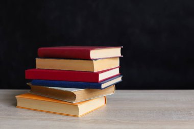 Koyu arkaplana karşı ahşap masadaki kitap yığını