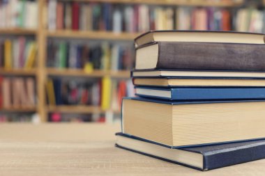 Tahta bir masada yığınla kitap.