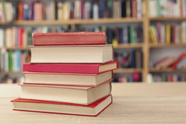 Kütüphane arkaplanına karşı ahşap masadaki kitap yığını