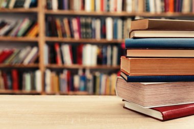 Fotoğraf, hem tanıdık hem de nazikçe idealize edilmiş gibi hissettiren sessiz bir sahne sunuyor: üzerinde açık bir kitap bulunan, pürüzsüz, soluk bir yüzey üzerinde dinlenen küçük bir kitap yığını, sayfaları çırpınışların ortasında kalmış.