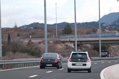 Split, Hırvatistan, 14.02.2026. Görüntü, az bitki içeren tepelik bir arazide yavaşça sağa doğru kıvrılan modern bir otoyolu gösteriyor. İki araba bitişik şeritlerdeki izleyiciden uzaklaşıyor, arka uçları açıkça görülüyor..