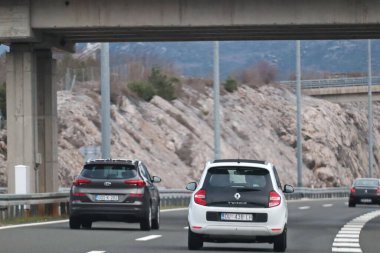 Split, Hırvatistan, 14.02.2026. Görüntü, az bitki içeren tepelik bir arazide yavaşça sağa doğru kıvrılan modern bir otoyolu gösteriyor. İki araba bitişik şeritlerdeki izleyiciden uzaklaşıyor, arka uçları açıkça görülüyor..