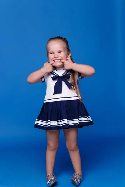 Full length portret van een klein geweldig meisje met blauwe ogen en het openen van de mond op een blauwe achtergrond. — Stockfoto