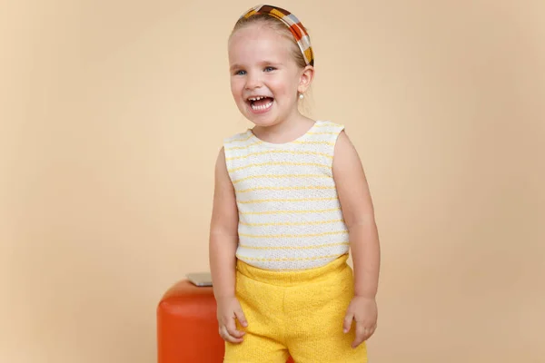 Schattig klein meisje met blauwe ogen, in gele wollen kleding, glimlachend aan een kant, op beige achtergrond, kopieerruimte. — Stockfoto