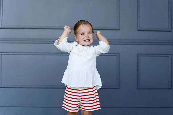 Het portret van een gefrustreerd klein meisje houdt haar handen omhoog, draagt een witte blouse en een rode broek. — Stockfoto