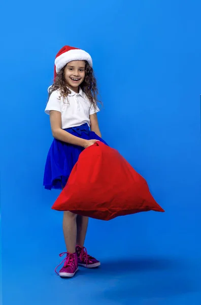 Framsidan porträtt av en liten lekfull glad flicka bär tomte hatt, isolerad på blå bakgrund. — Stockfoto