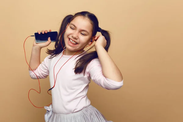 Söt liten flicka lyssnar musin på sina hörlurar, med slutna ögon, poserar i studio, på beige bakgrund. — Stockfoto