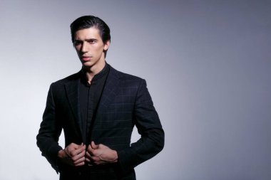 Gri arka planda izole edilmiş siyah takım elbiseli yakışıklı bir gencin ön portresi. Metin için boşluk.