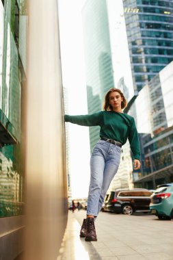 Kendine güvenen hippi kız, kısa sarı saç stili, mavi giyinmiş, kot pantolon, botlar, gün batımında arka planda..