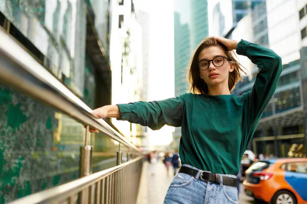 Retrato frontal de uma menina com penteado curto, olhando para a câmera, posando na rua urbana, prédios fundo. — Fotografia de Stock