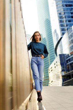 Sarı saçlı hippi kız, kot pantolon, bot giyiyor, gün batımında sokak duvarına karşı poz veriyor..