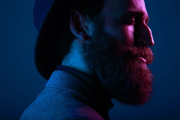Крупный план портрета бородатого человека в шляпе и костюме, с закрытыми глазами, позирующими в профиль, на темно-синем фоне. — стоковое фото