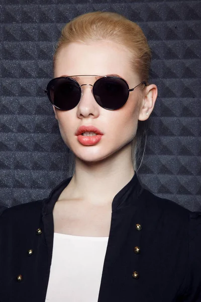 Frontporträt eines sexy blonden weiblichen Modells mit Make-up und Pferdeschwanzfrisur, das schwarze Jacke und Sonnenbrille trägt. — Stockfoto
