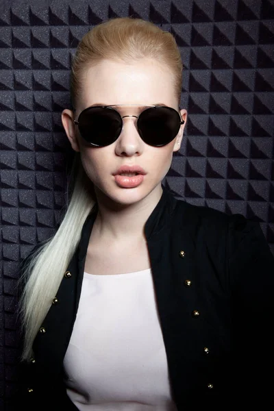 Első kép egy érzéki szőke nő modell smink és lófarok frizura, visel fekete kabát és napszemüveg. — Stock Fotó