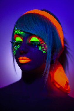 Artistik makyajlı, turuncu eşarplı, izole menekşe mavisi arka planı olan bir kızın UV ön portresini kapat..