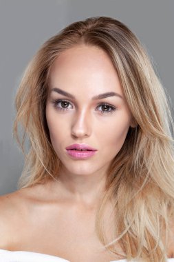 Gri arka planda güzel makyajlı, şehvetli sarışın bir kadının ön portresi..
