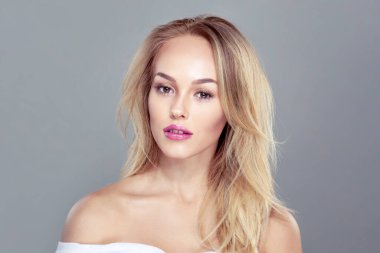 Güzel makyajlı, açık gri arkaplan üzerinde çıplak omuzları olan neşeli, seksi sarışın bir kadının yakın plan görüntüsü..