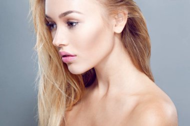 Profilde güzel makyajlı, açık gri arka planda uzun saçlı, neşeli, seksi sarışın bir kadın resmi var..