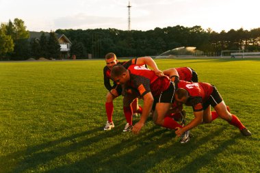 Spor ekipmanlı bir grup adam dışarıda bir spor sahasında rugby oynuyor..