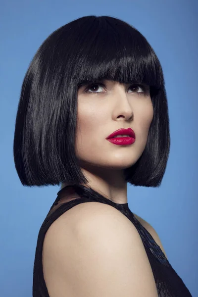 Nahaufnahme Schönheit Porträt einer brünetten Frau in schwarzer Perücke mit Make-up, roten Lippen, über blauem Hintergrund. — Stockfoto
