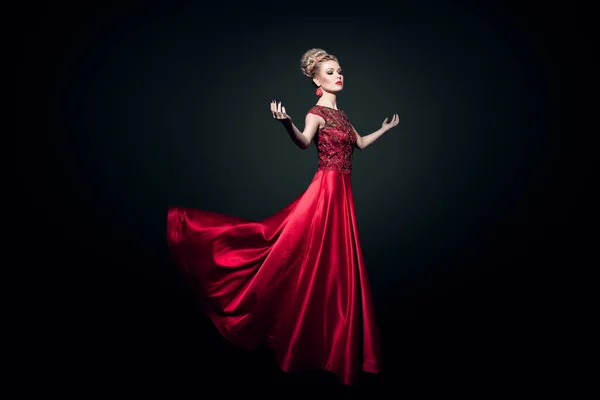 Fulll vista de longitud de una maravillosa mujer joven dressd en un largo vestido rojo con las manos levantadas, sobre fondo negro. — Foto de Stock