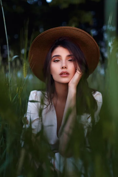 Carefree adorable brunette young woman in romantic outfit, with hand on her face in green field. Care concept. — Stock Photo, Image